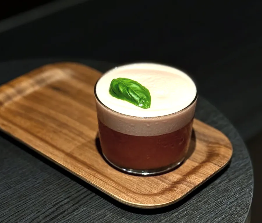 A D.O.S.E foamed coffee with a fresh green leaf on a wooden tray